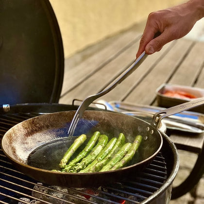Matlagningsgaffel med sparris på kolstålspanna på en grill